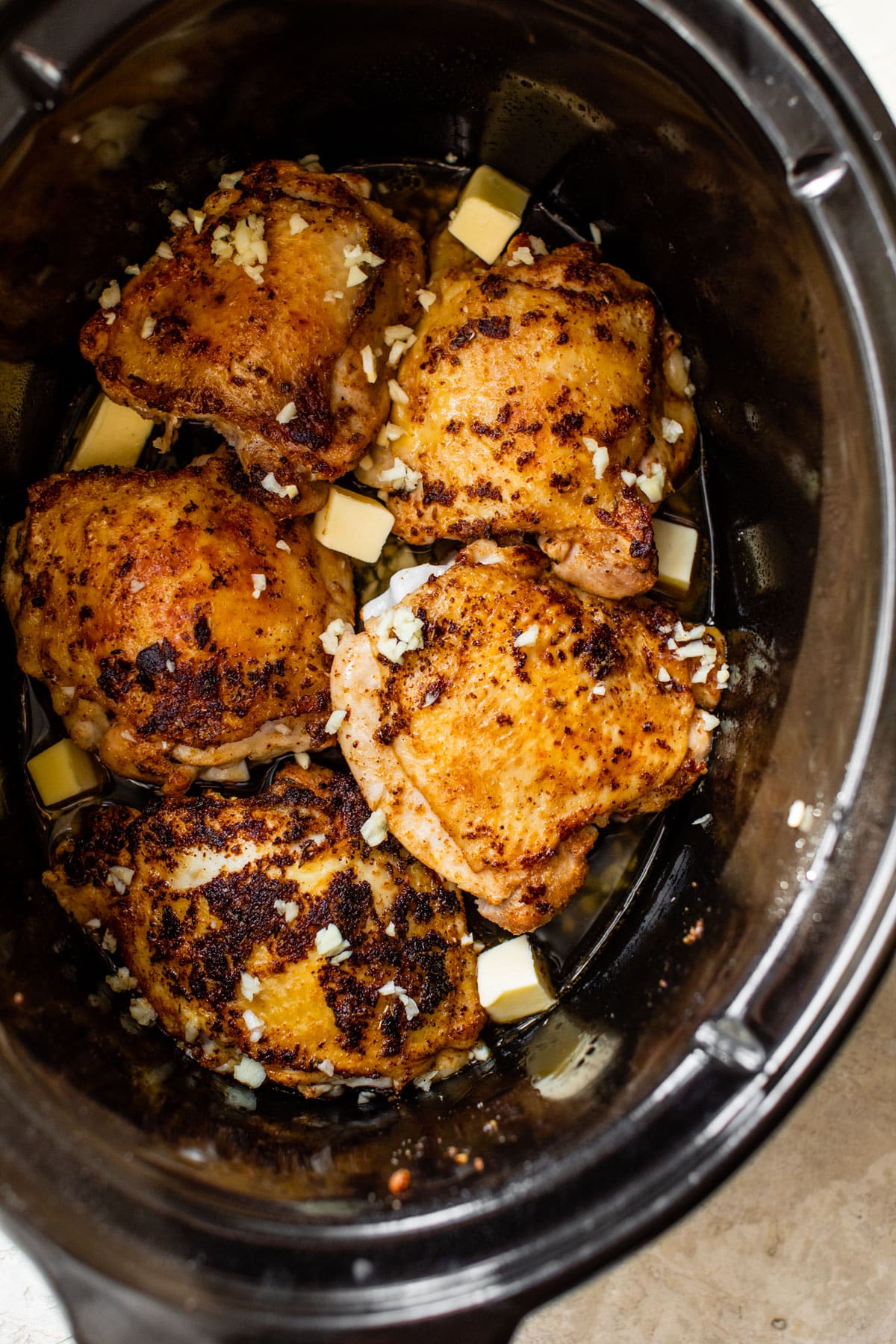 raw chicken thighs in a slow cooker with cubes of butter