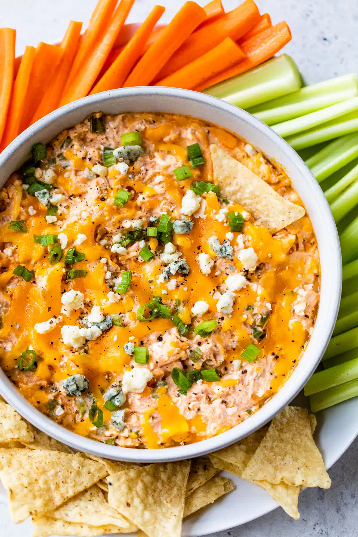 a bowl of chicken dip surrounded by tortilla chips, celery and carrots