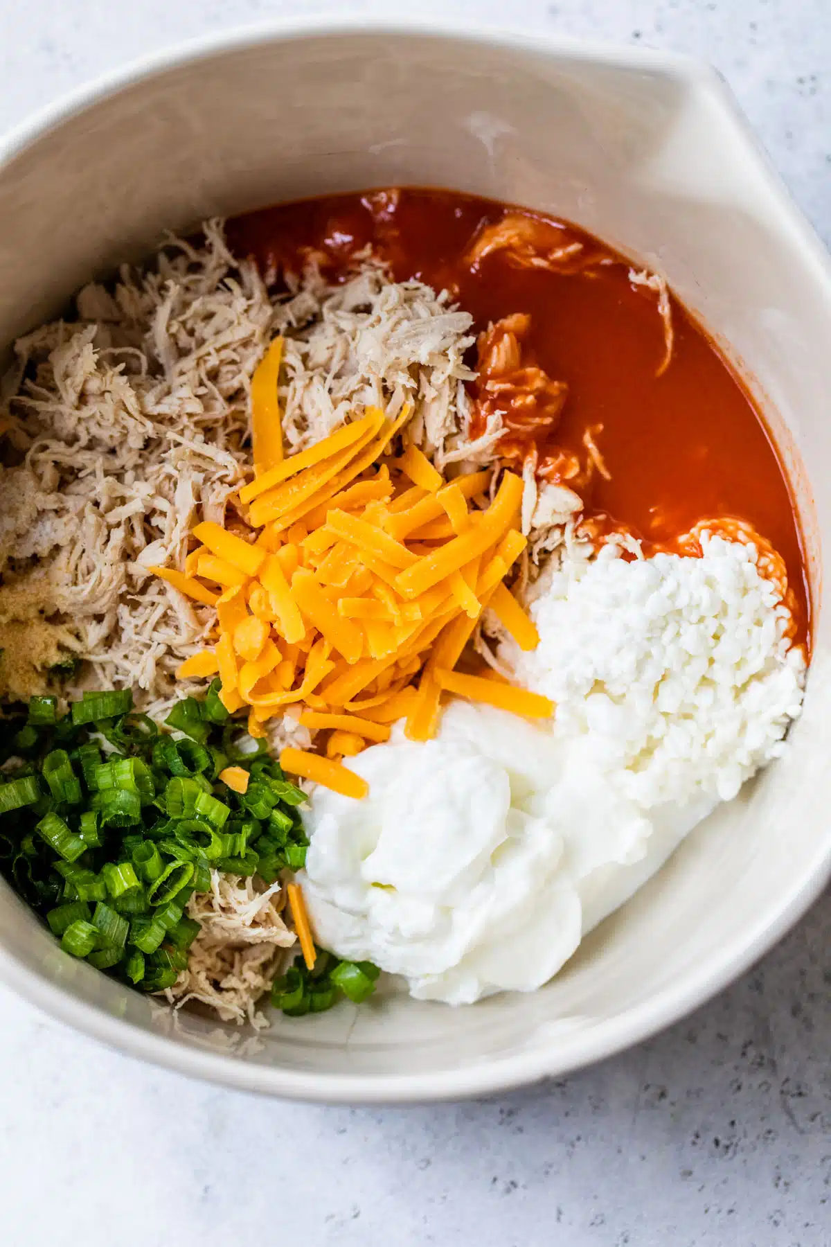 a bowl filled with shredded chicken, hot sauce, cheddar cheese, green onion, and yogurt