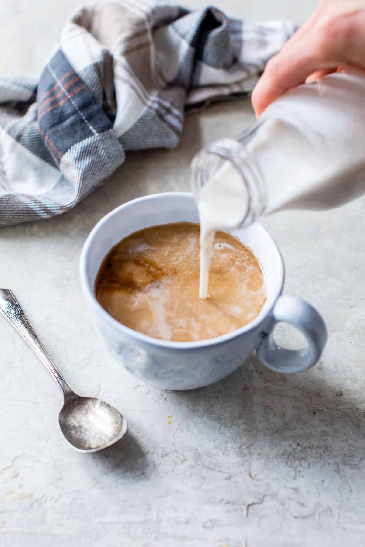 someone pouring coffee creamer into a mug of coffee