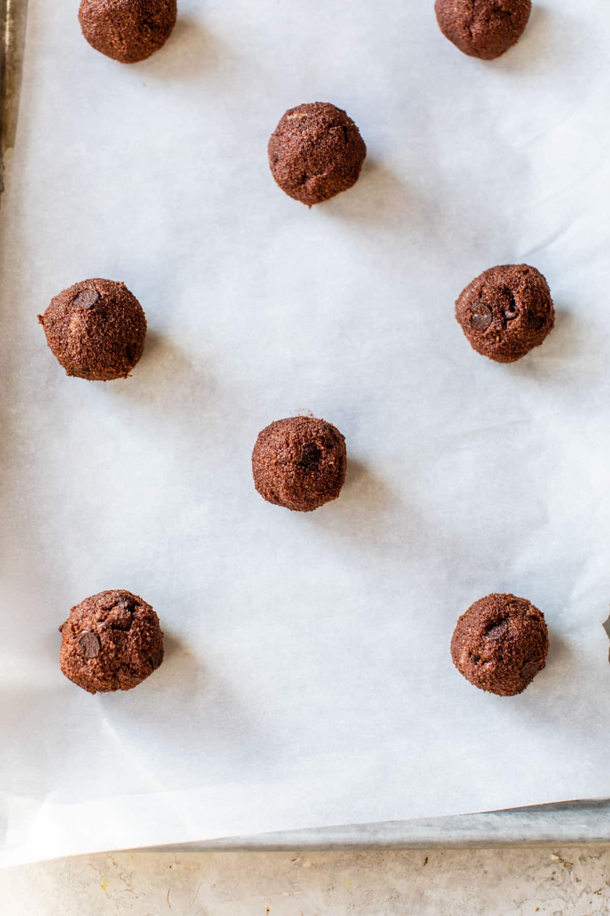 chocolate balls of cookie dough on a parchment-lined baking sheet