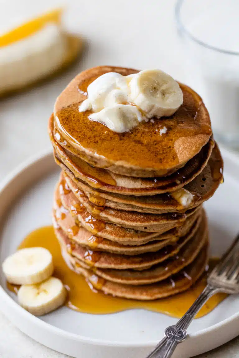stack of pancakes on a plate topped with yogurt and banana