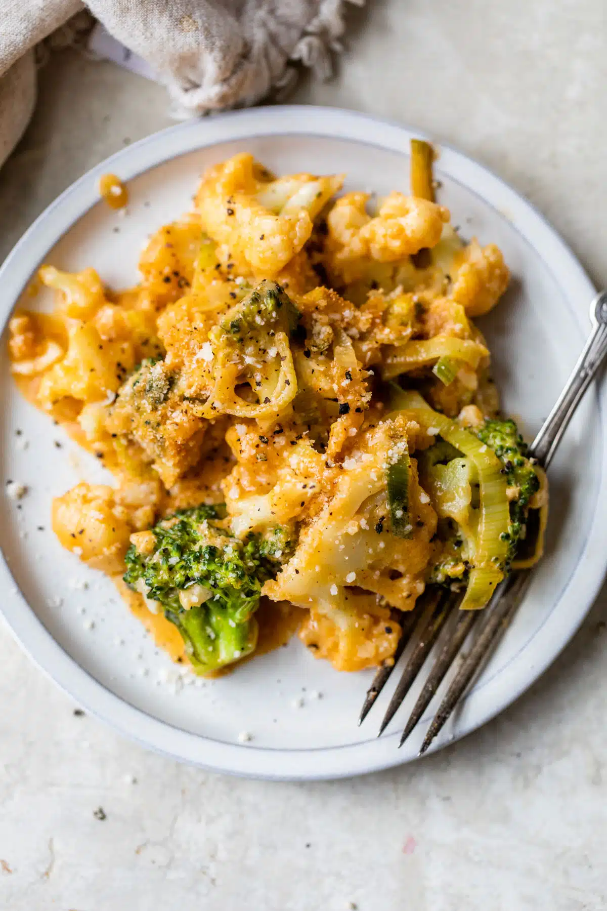 a plate of broccoli and cauliflower coated in a cheese sauce with a fork