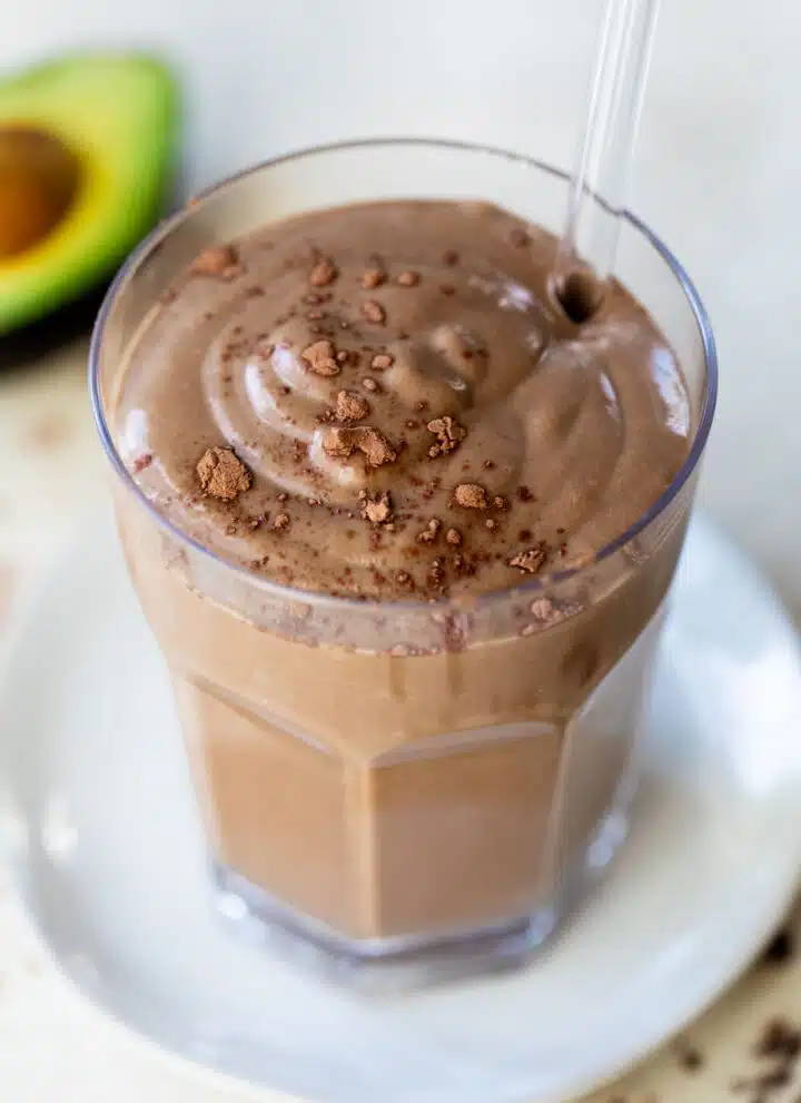 chocolate smoothie in a glass with a straw beside an avocado