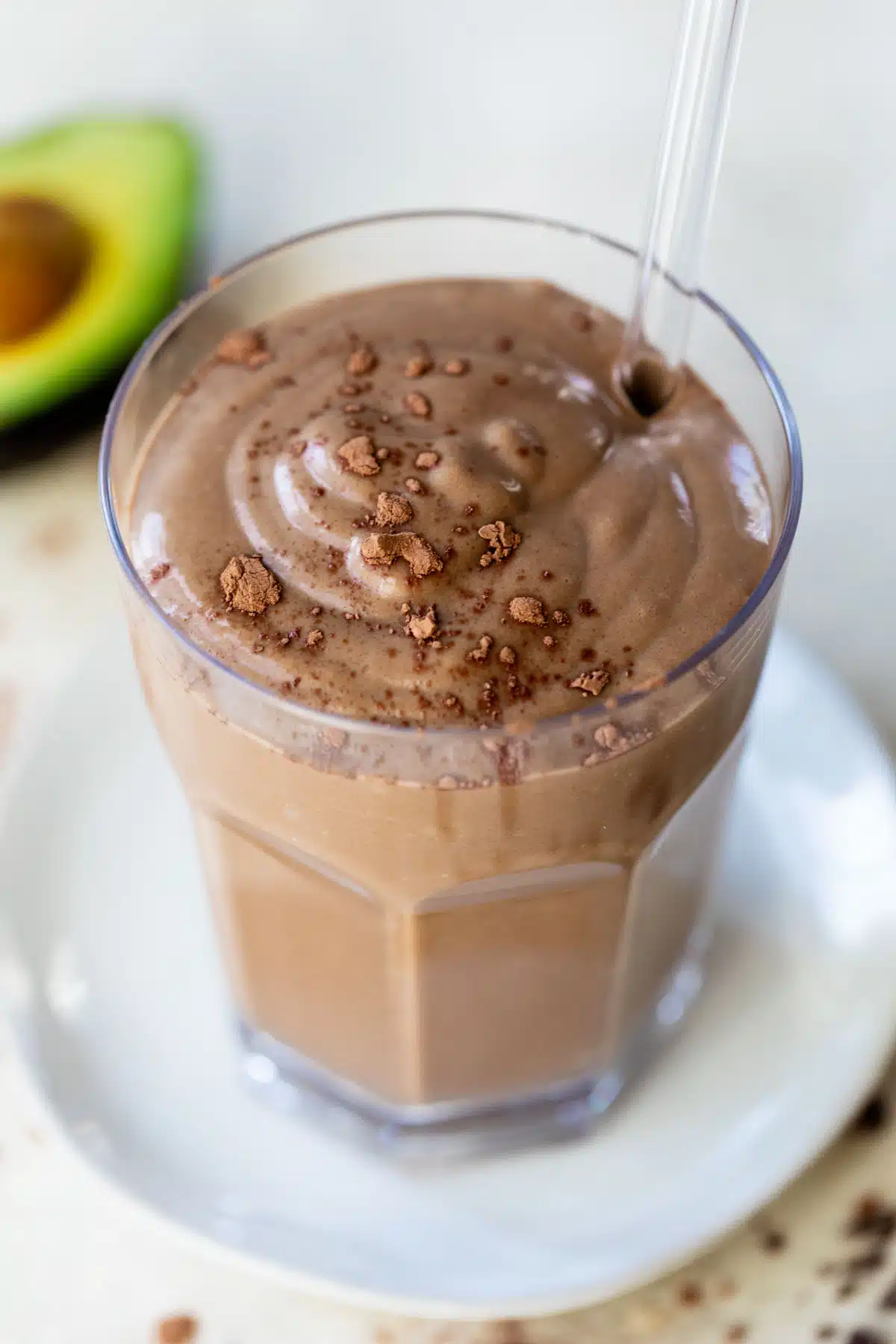 chocolate smoothie in a glass with a straw beside an avocado
