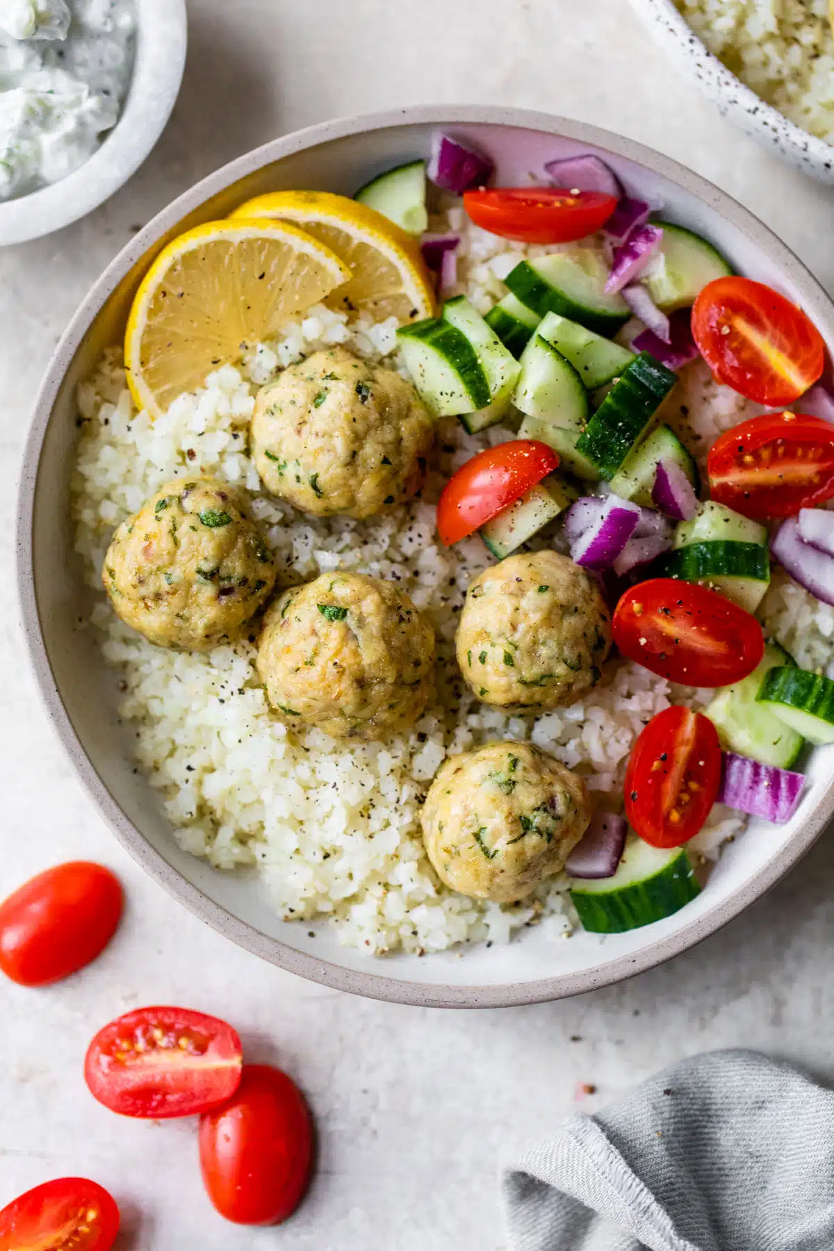 cauliflower rice topped with meatballs and vegetables like tomatoes and cucumber in a bowl