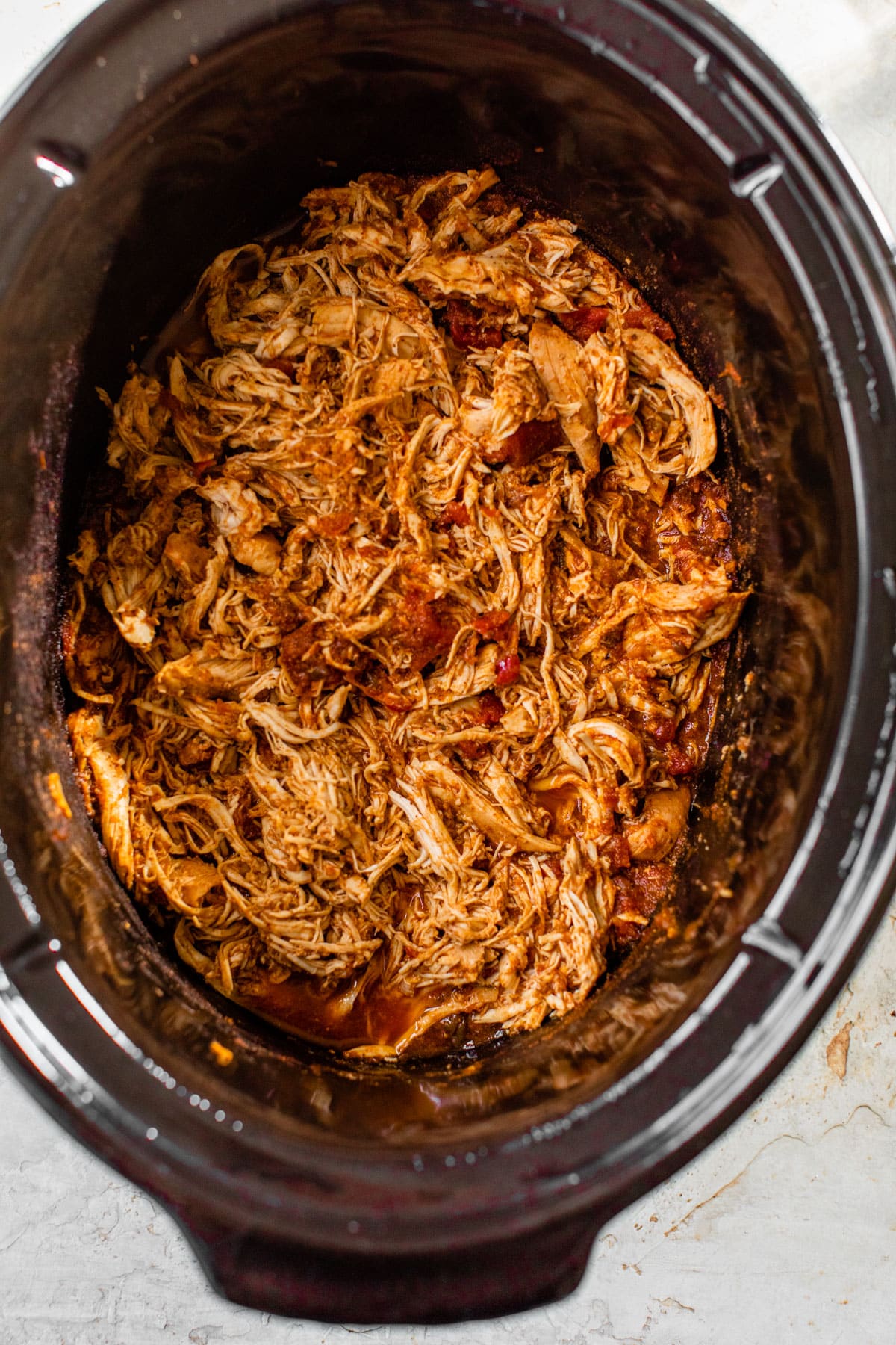 shredded cooked chicken in a red sauce in the crockpot