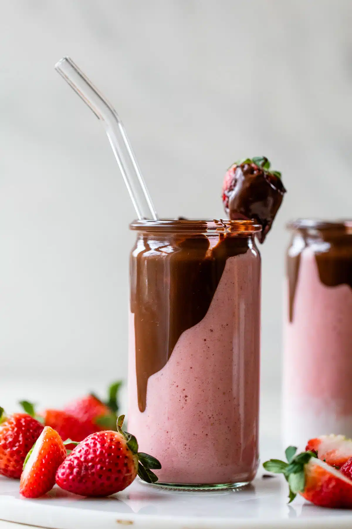 glass filled with a pink-colored smoothie with chocolate on the inside and a chocolate covered strawberry on top