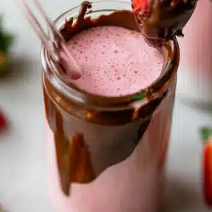 tall glass with chocolate on the inside of it filled with a strawberry smoothie
