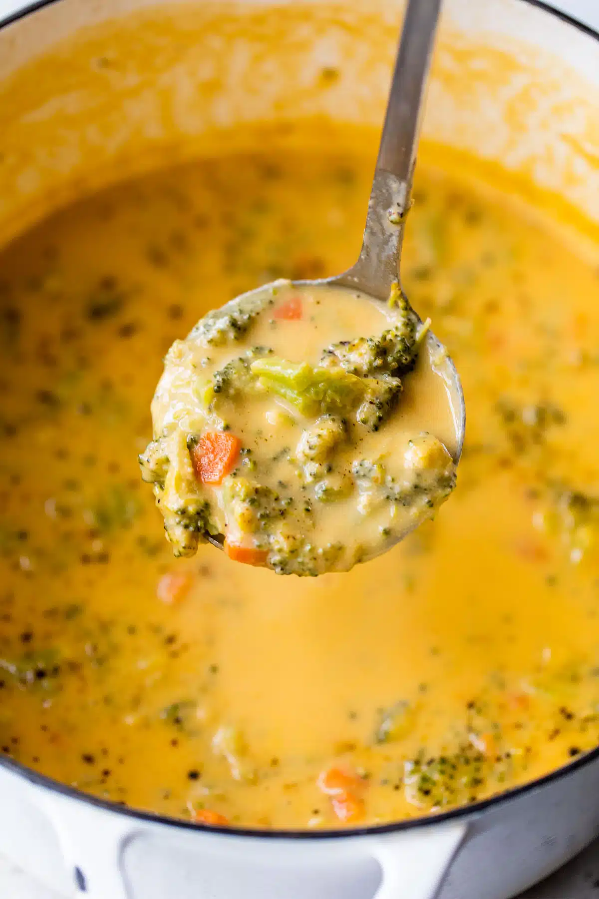 a ladle full of broccoli cheddar soup with the pot of soup beneath it