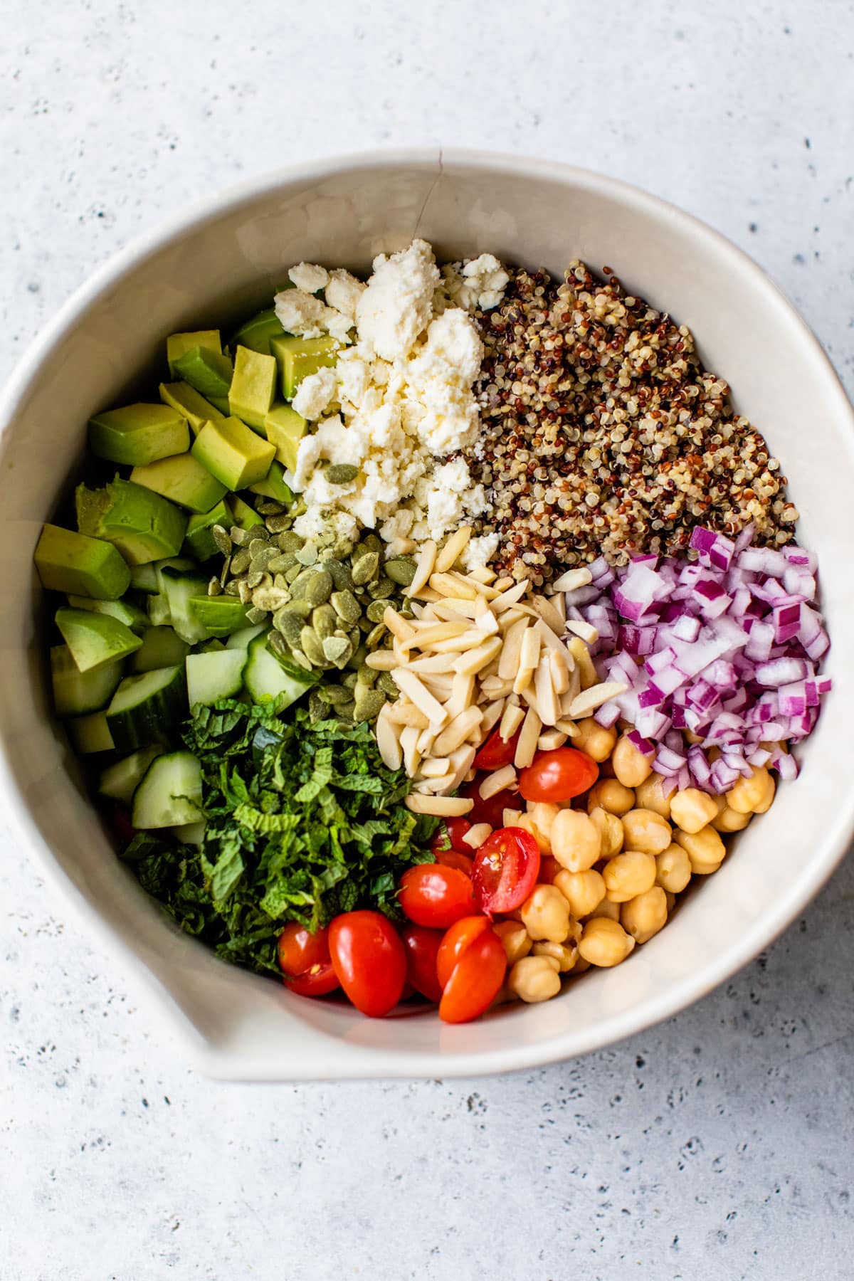 bowl with quinoa, feta cheese, cucumber, and other vegetables inside