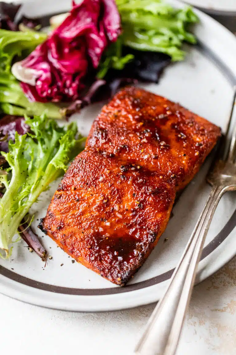 zoomed in image of cooked salmon on a plate with lettuce and a fork