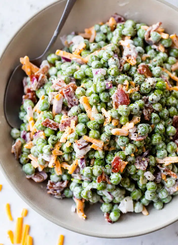 green pea salad in a bowl with bacon, cheese and a spoon