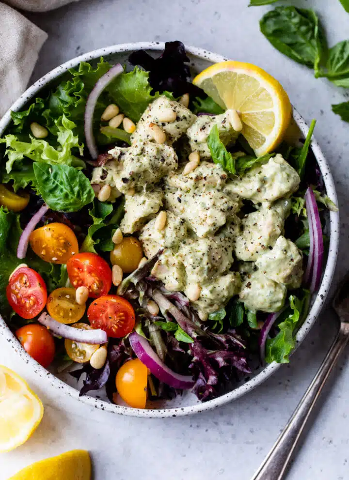 a salad with pieces of pesto covered chicken on top