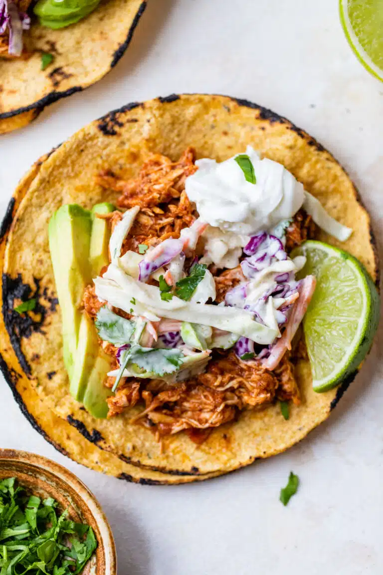 corn tortillas topped with shredded chicken, slaw, avocado, and a lime wedge