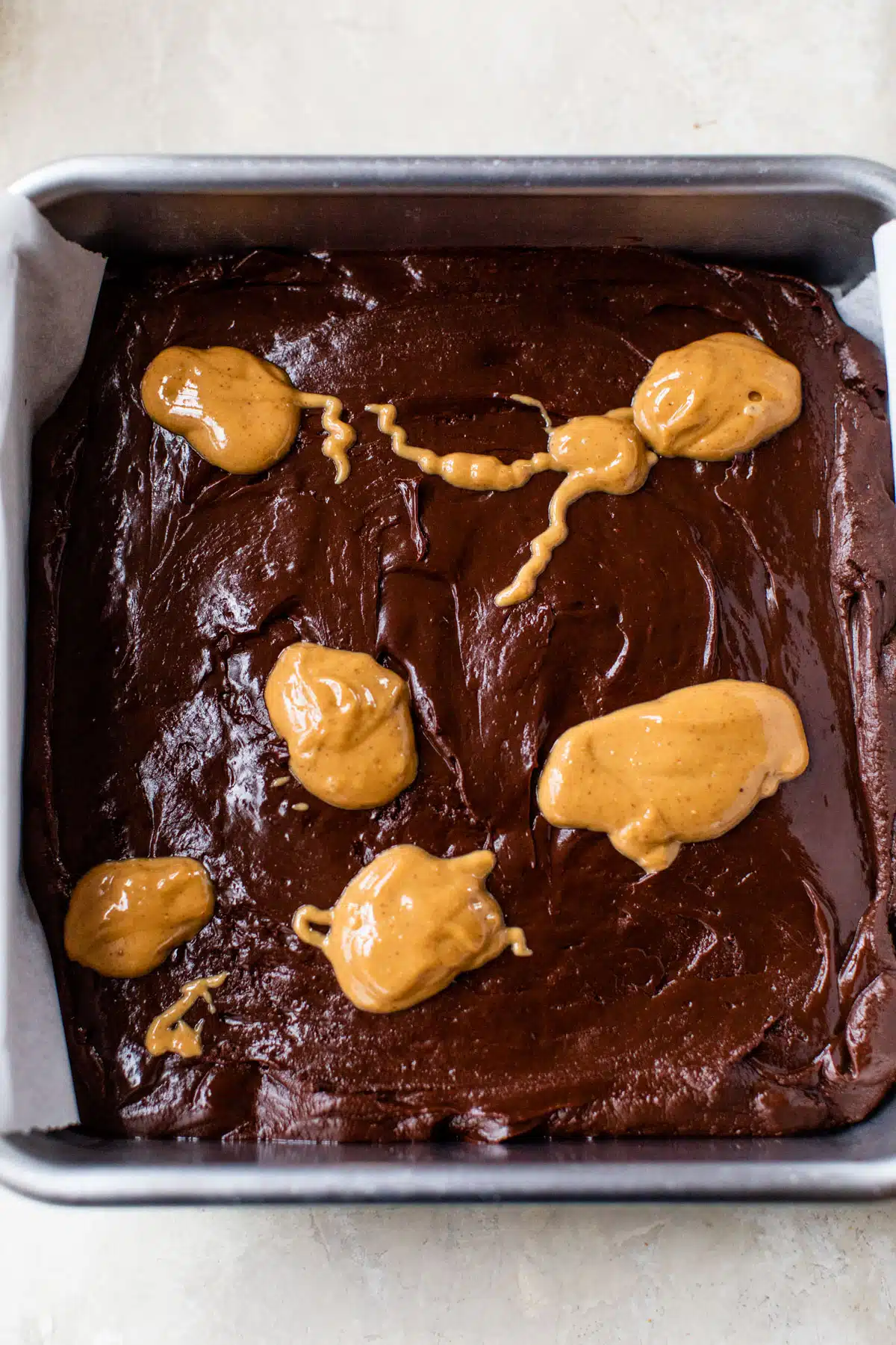 chocolate mixture in a square baking pan with dollops of peanut butter overtop