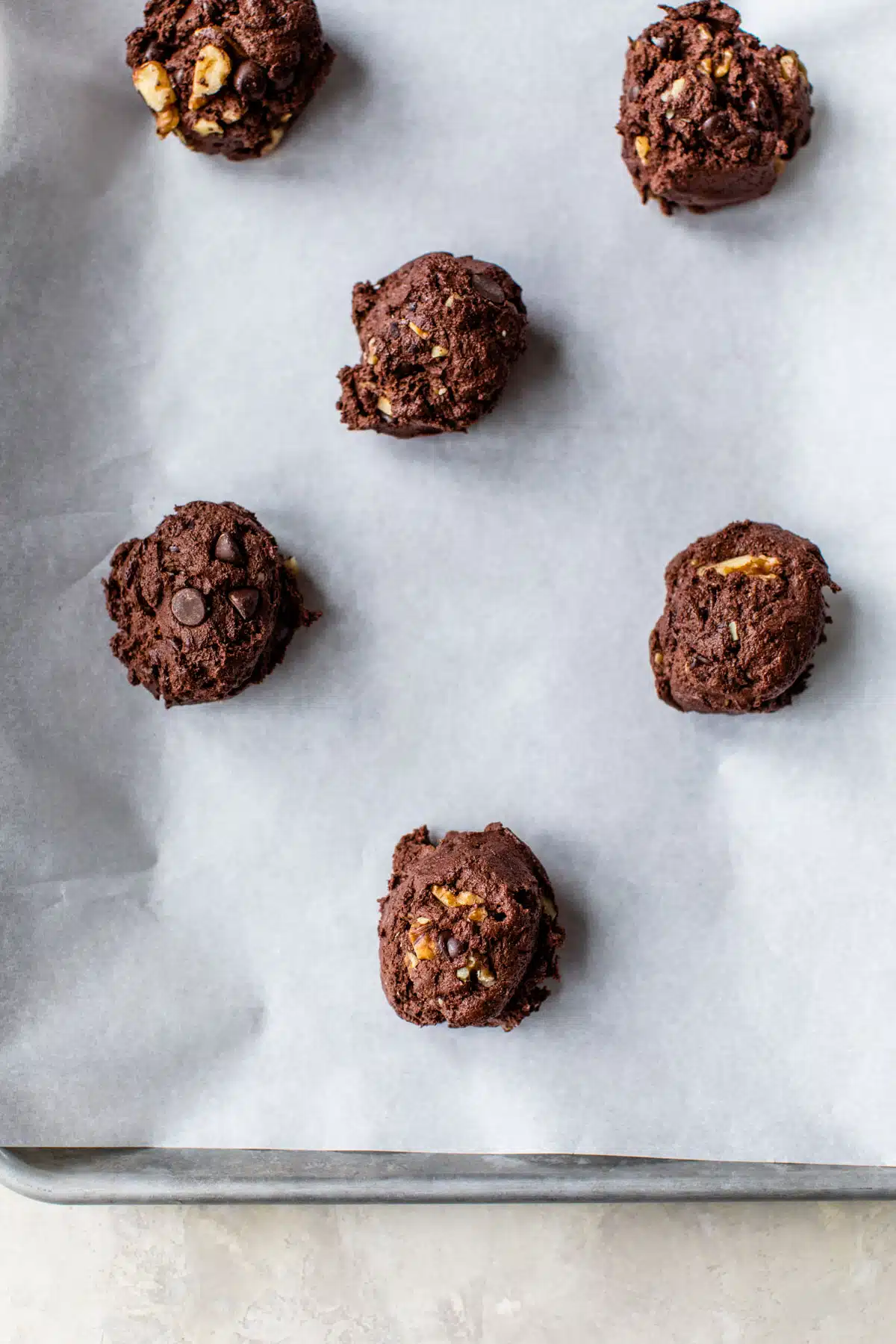 raw chocolate cookie dough balls on a parchment-lined baking sheet