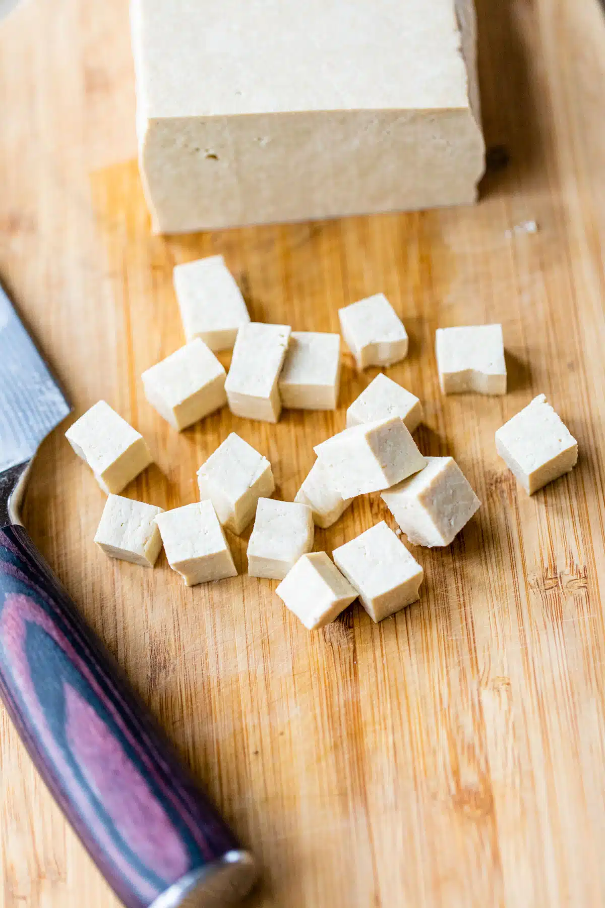 a block of tofu with cubes sliced from the block on a cutting board