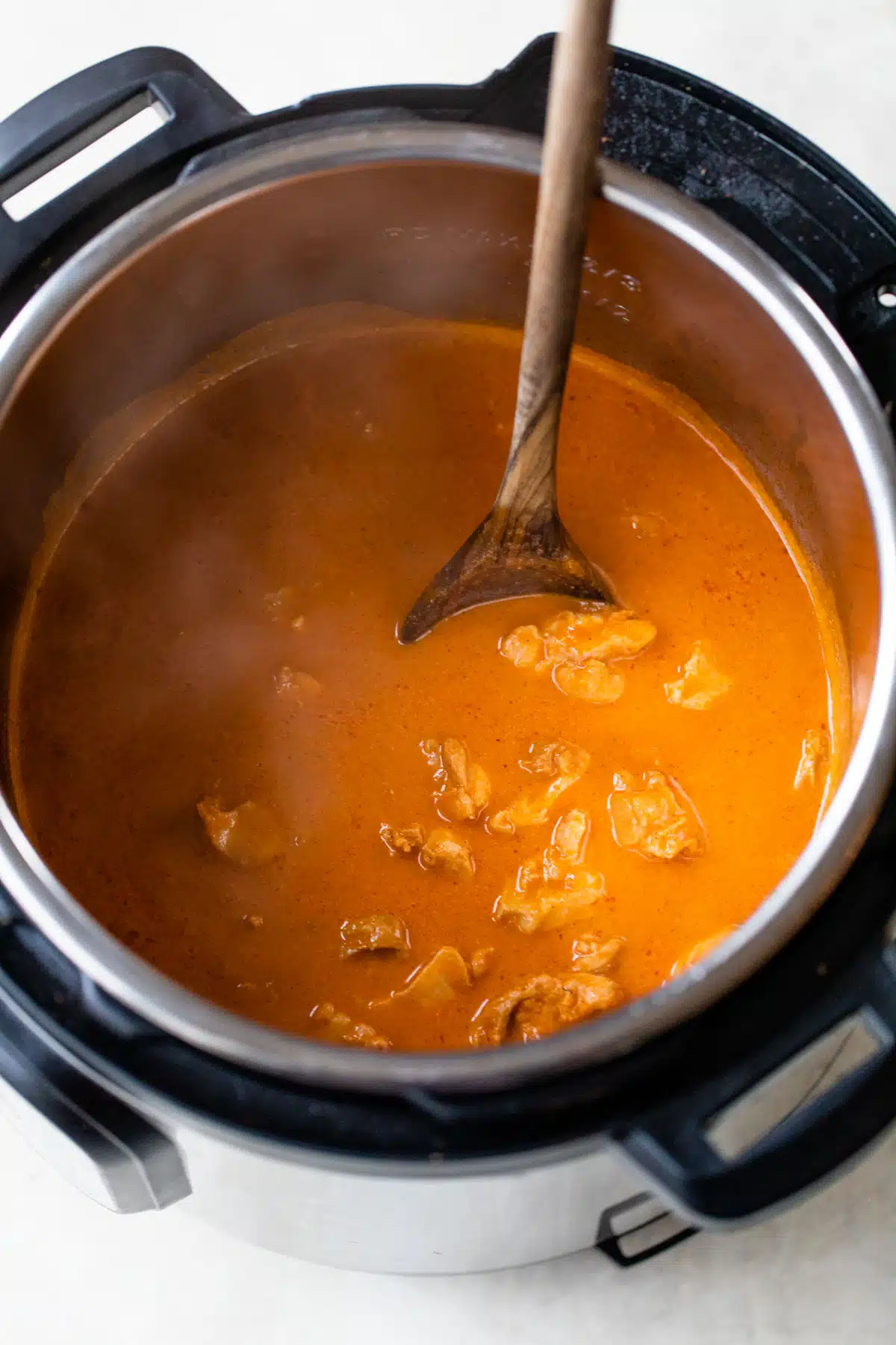 an instant pot with chicken, butter, and water inside with a wooden spoon
