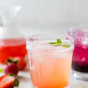 two cocktail glasses with fruity drinks in them besides fresh strawberries and fresh blackberries