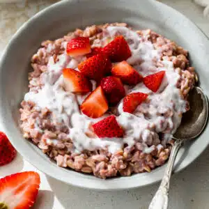 a bowl of pink-colored oats topped with yogurt and chopped strawberries