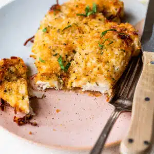 baked parmesan chicken with a bite taken out on a plate with a fork
