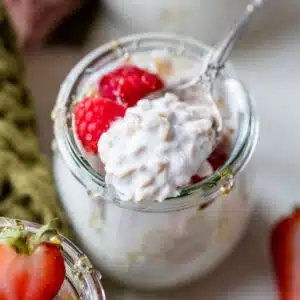 a spoonful of overnight oats in a mason jar with raspberries on top