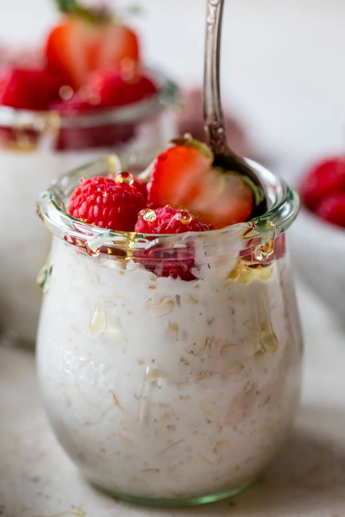 overnight oats in a mason jar with a spoon with raspberries and strawberries on top