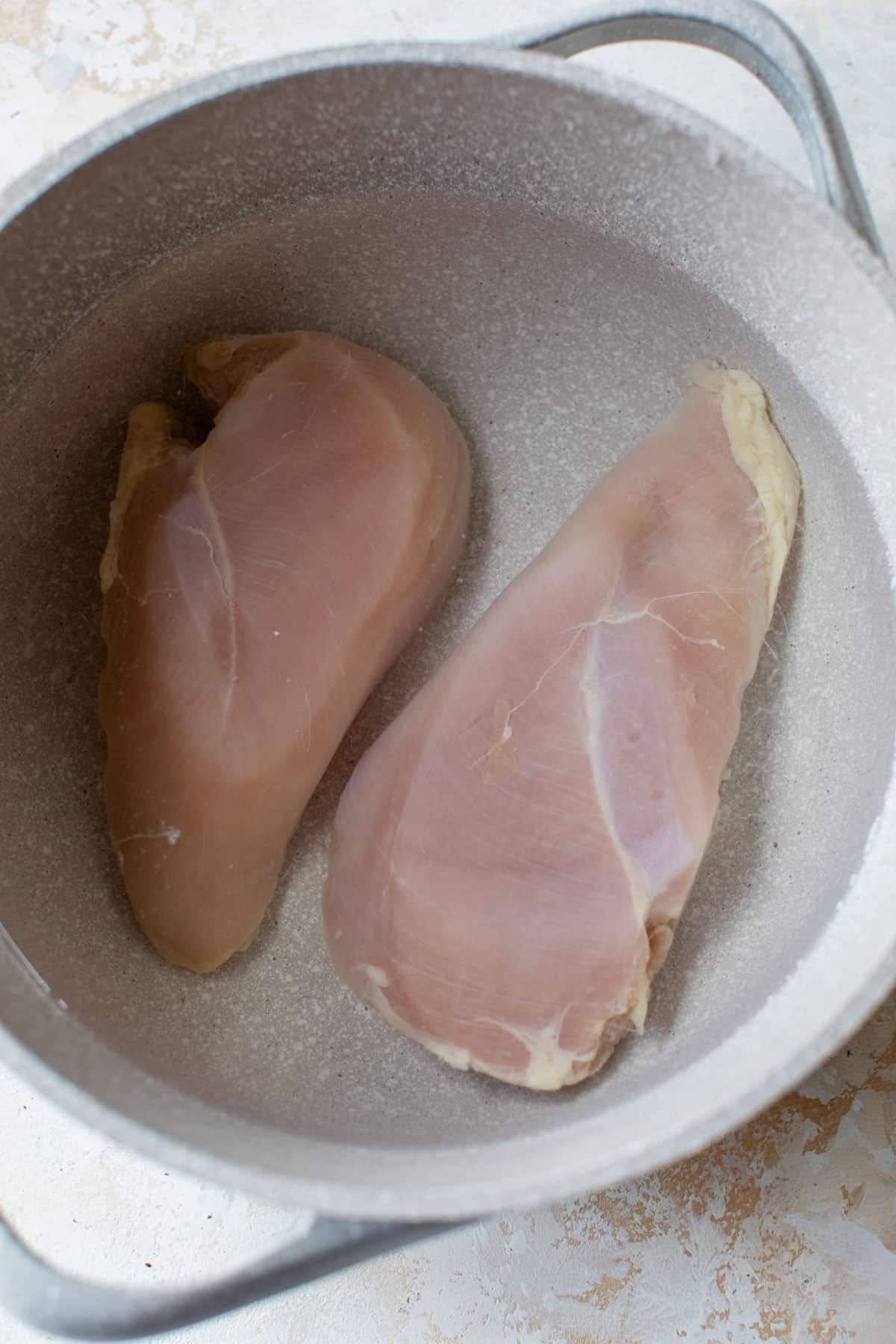 2 chicken breasts inside of a pot with water
