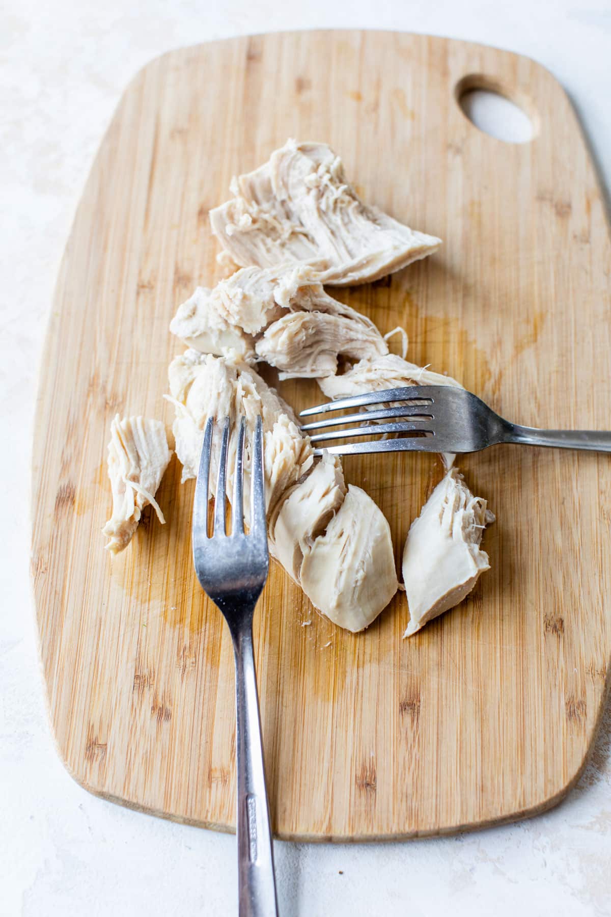 chicken being shredded by forks on a cutting board