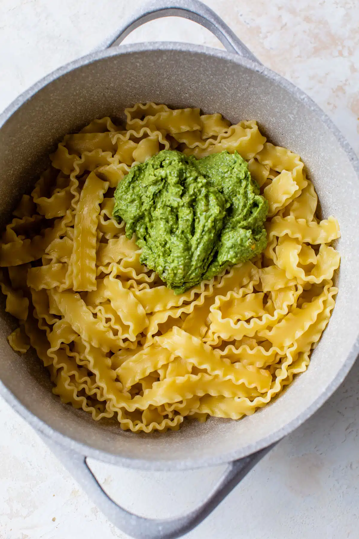 noodles inside of a large pot with avocado pesto added on top of the noodles