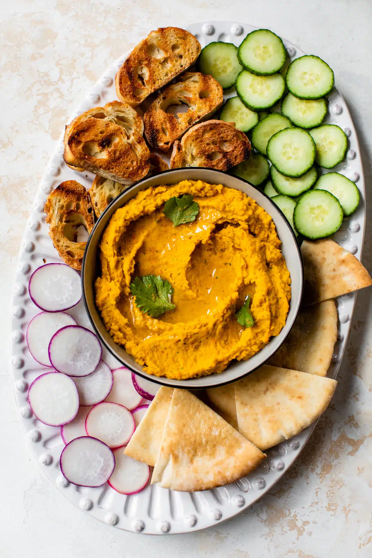 an overview of a platter with carrots hummus in a bowl surrounded by pita and veggies