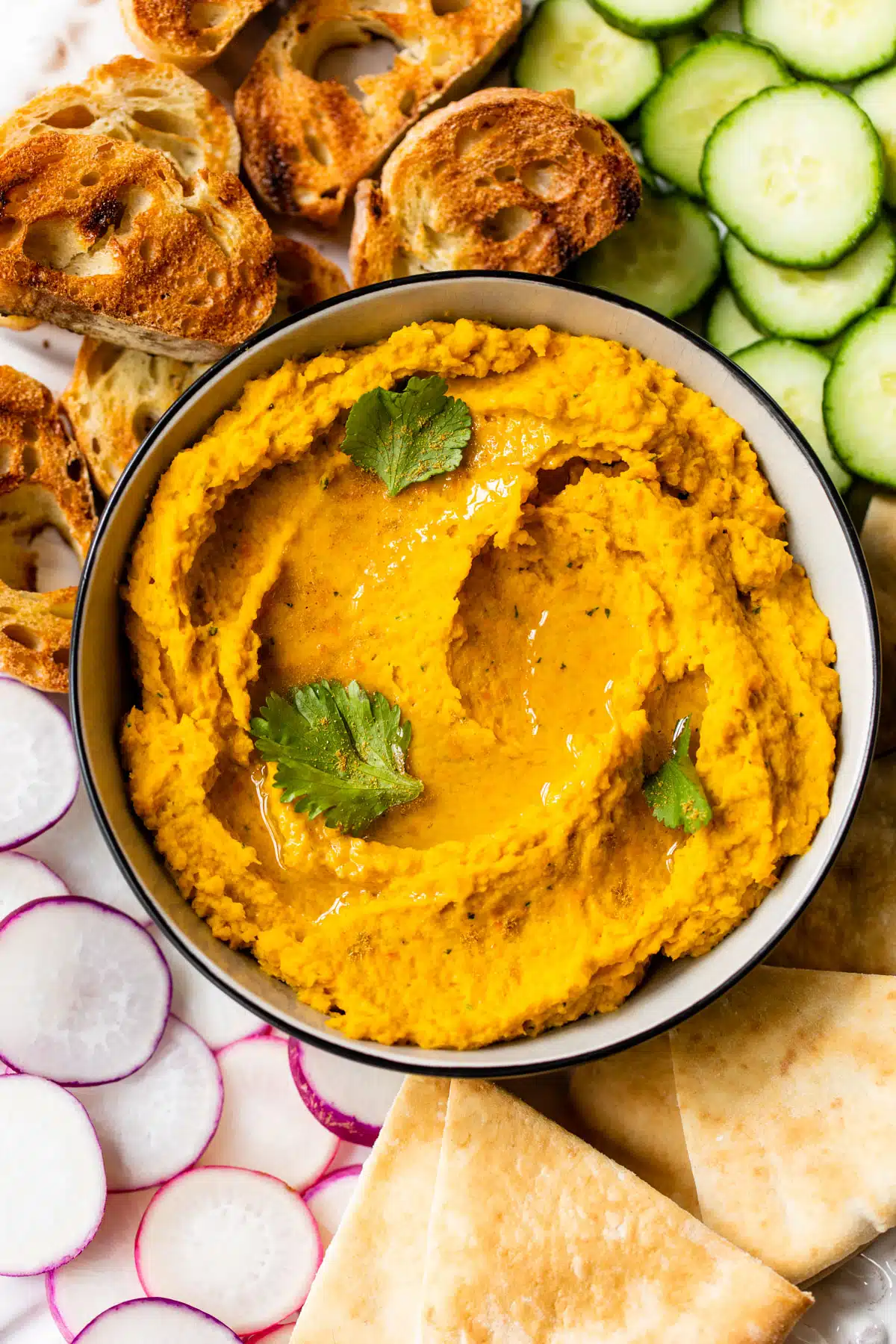 an overview of carrots hummus in a bowl surrounded by pita and veggies