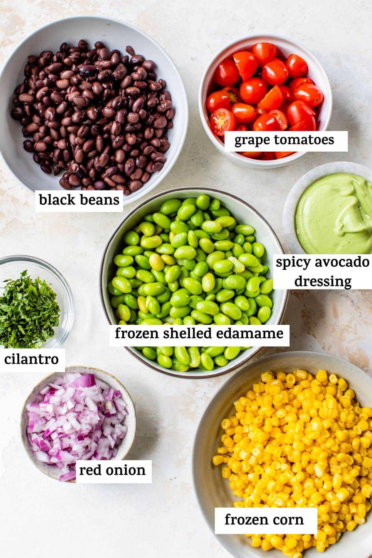 all of the ingredients for the edamame salad in bowls with text showing which ingredient is which