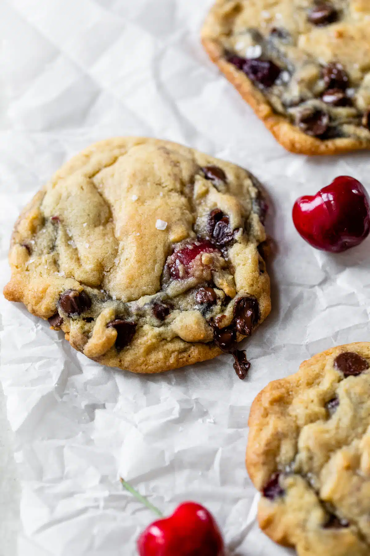 chocolate chip cookies on parchment paper with fresh cherries