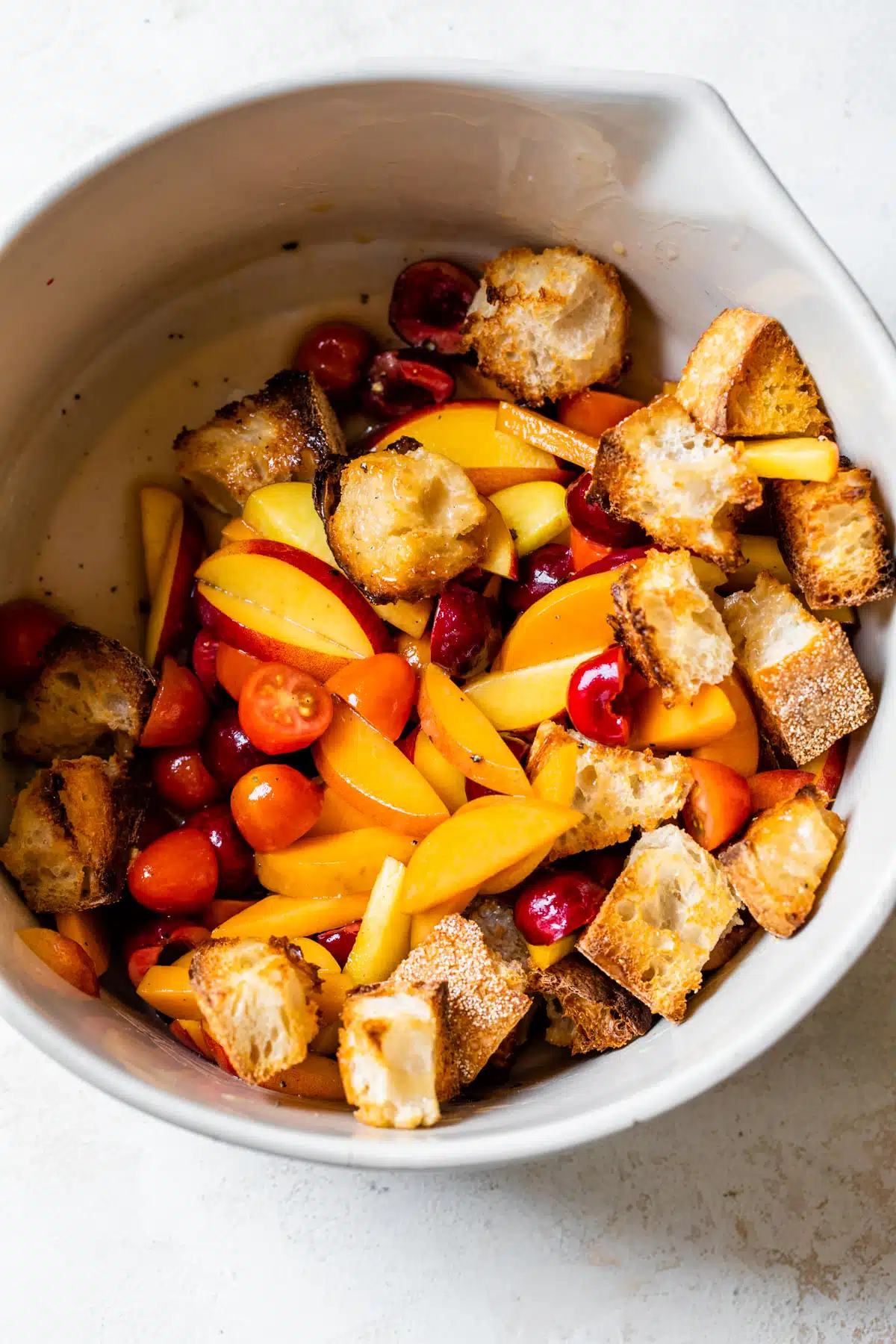 a large bowl filled with peaches, cherries, tomatoes, and toasted bread cubes