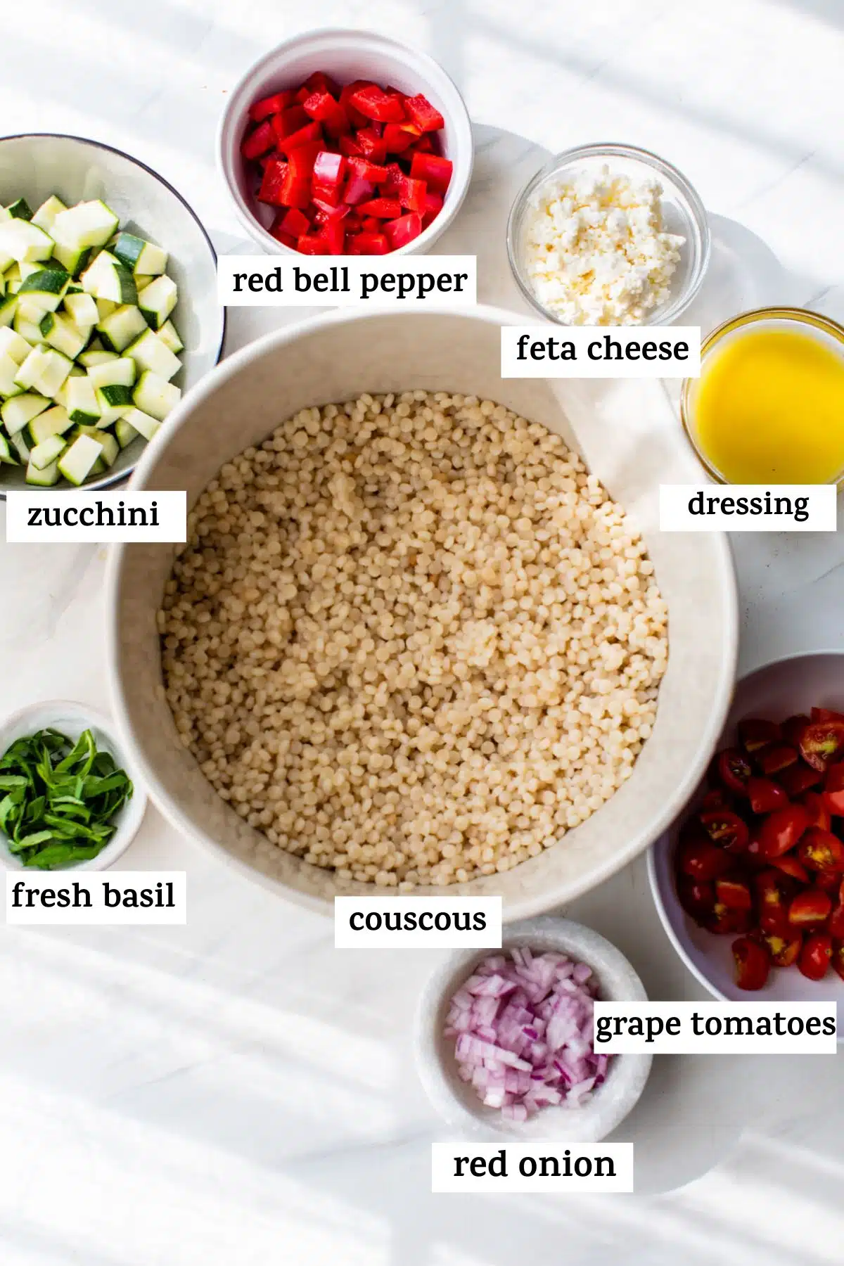 all of the vegetable couscous ingredients in bowls on a counter with labels showing what is in each bowl