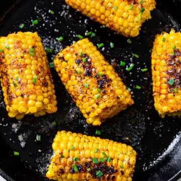 charred ears of corn in a skillet topped with chopped chives