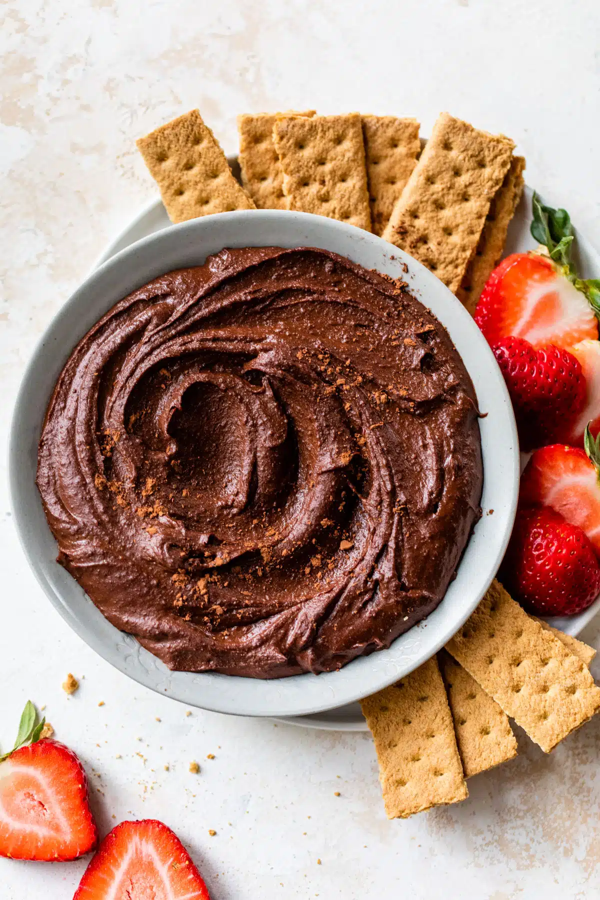 a bowl of chocolate hummus surrounded by graham crackers and sliced strawberries