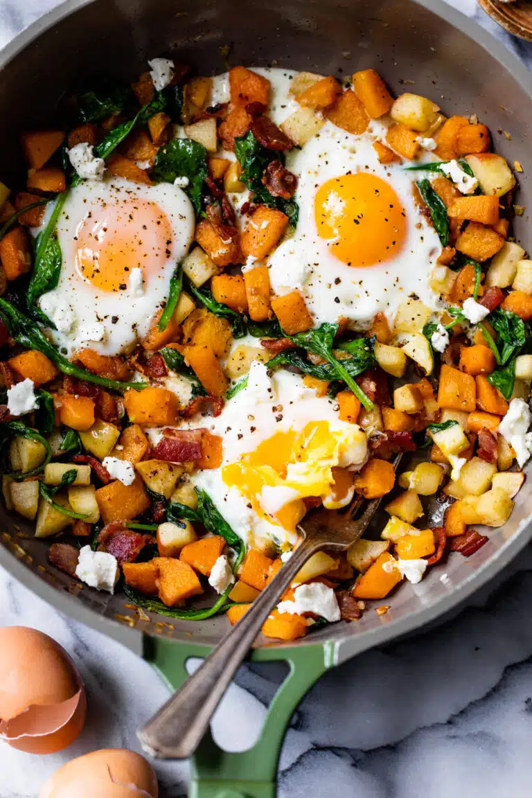 butternut squash hash with 3 eggs in a skillet with a fork