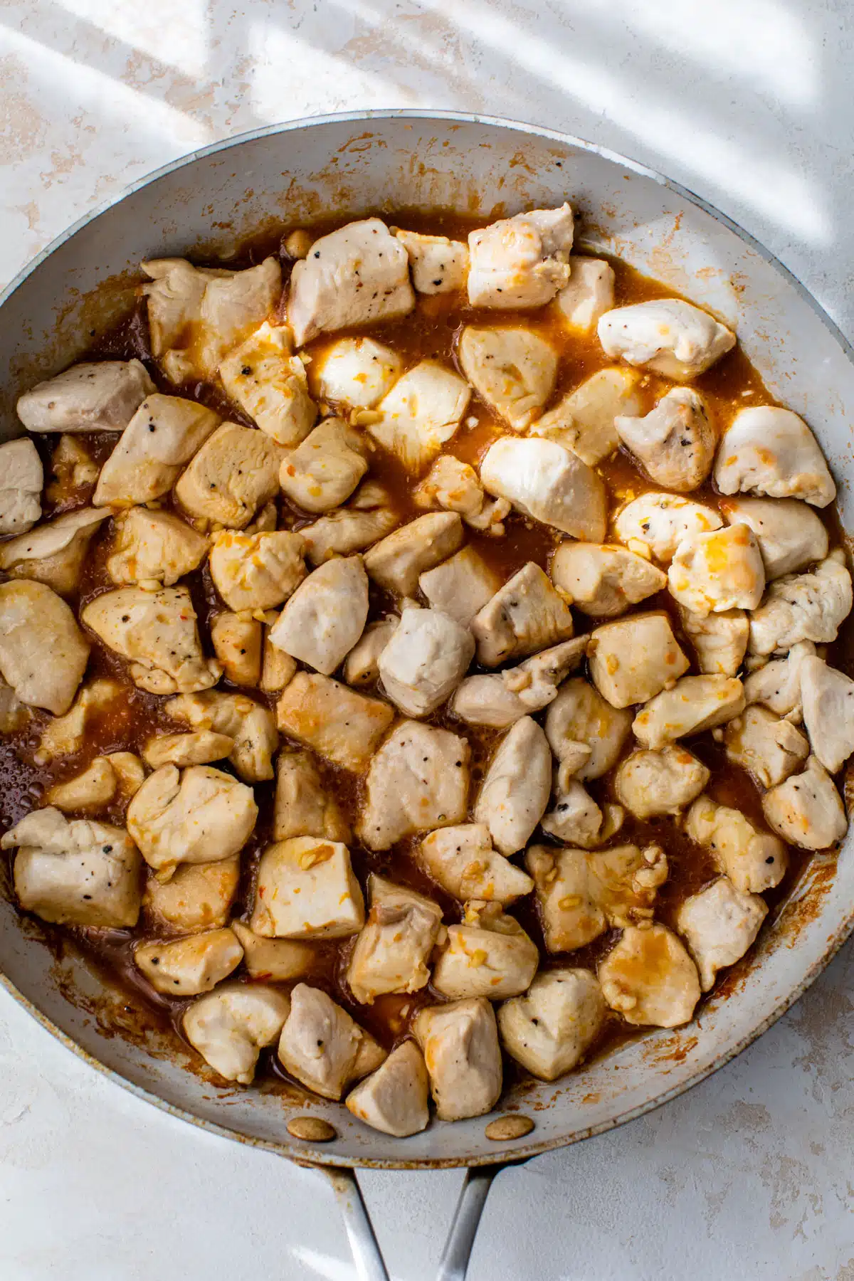 chicken pieces cooking in a skillet with sauce poured over the top