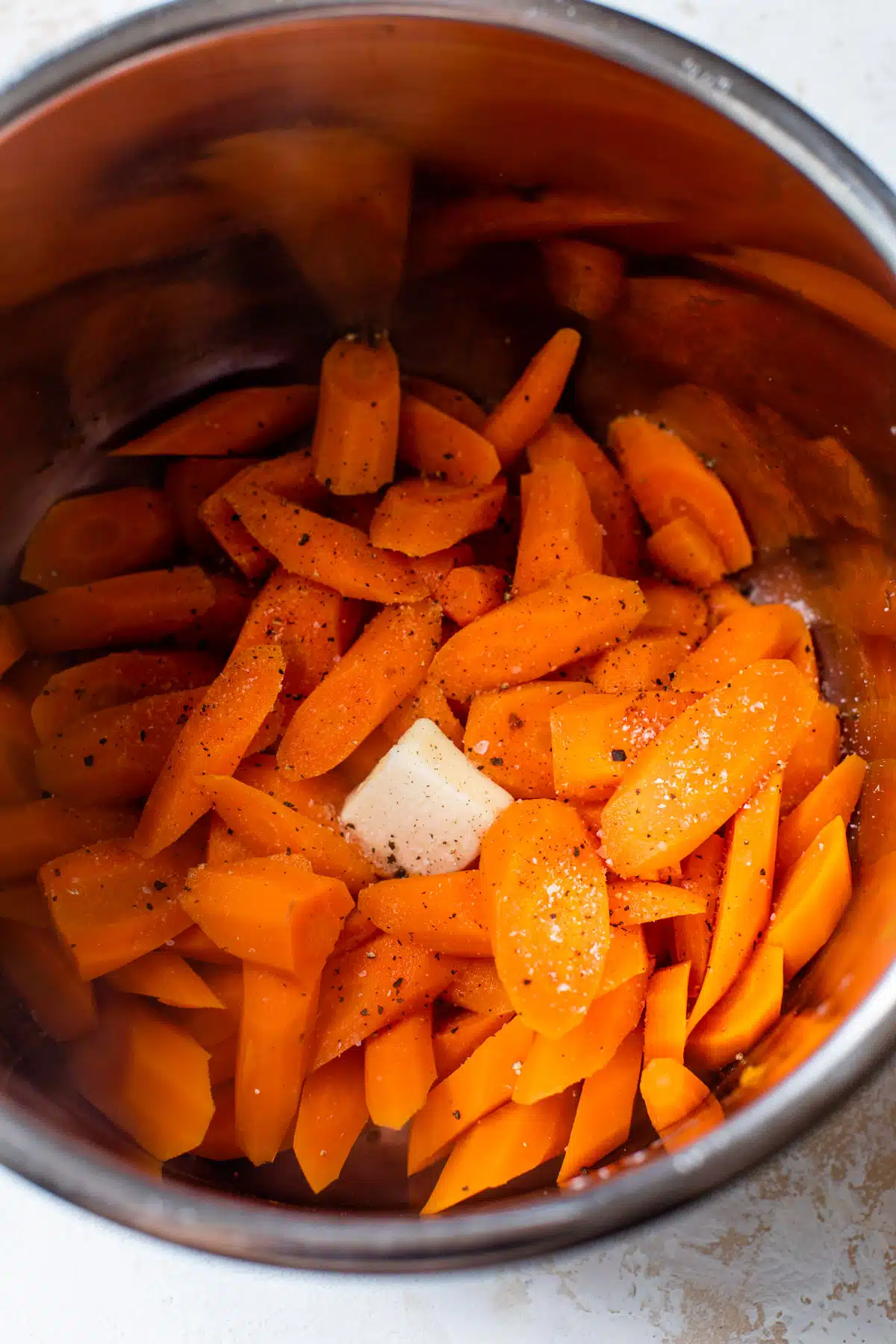 sliced carrots inside an instant pot with salt, pepper, and butter