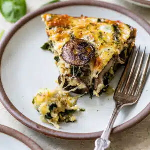 a slice of spinach mushroom quiche on a plate with a fork