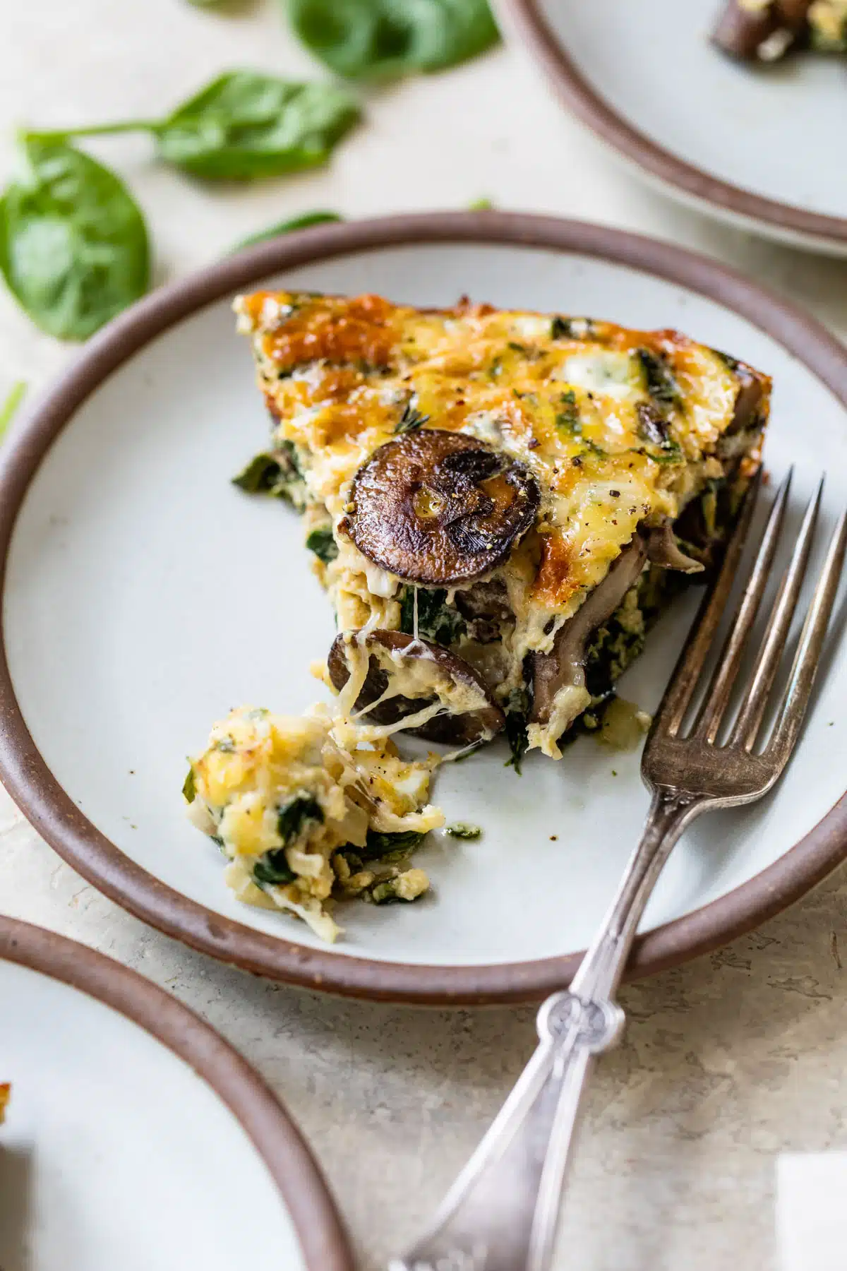 a slice of spinach mushroom quiche on a plate with a fork