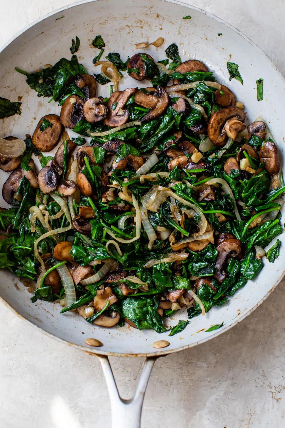 spinach, mushrooms, and onion cooking in a skillet
