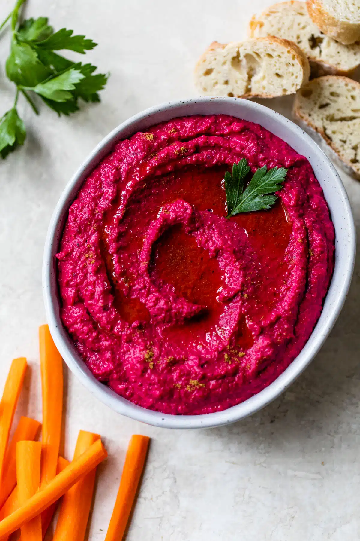 beet hummus in a bowl surrounded by slices of bread and carrots