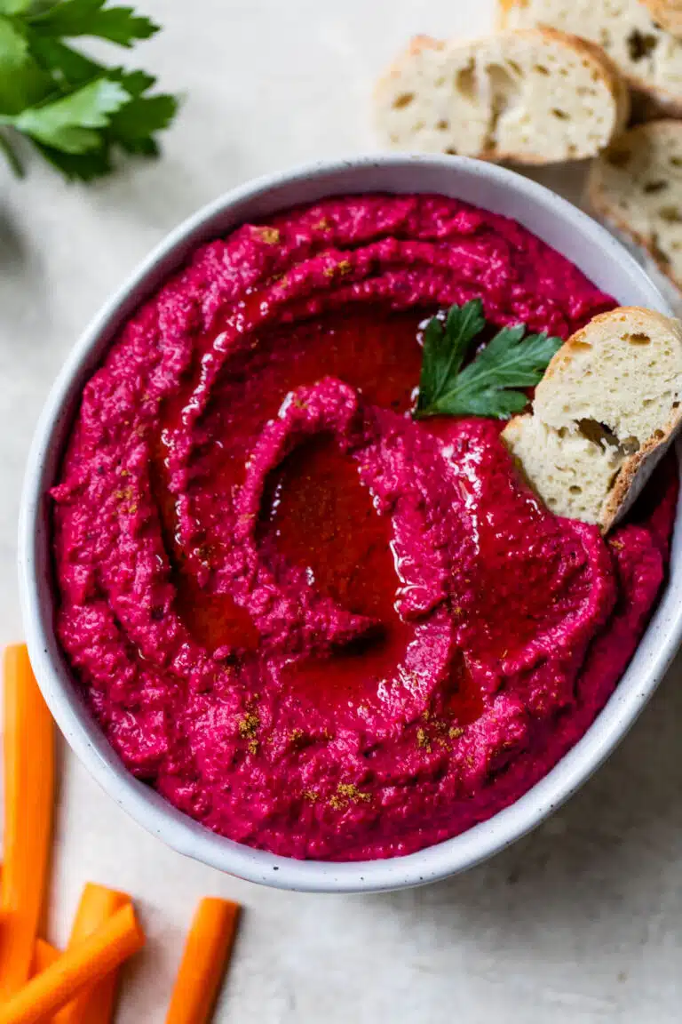 beet hummus in a bowl with a slice of bread on top and bread