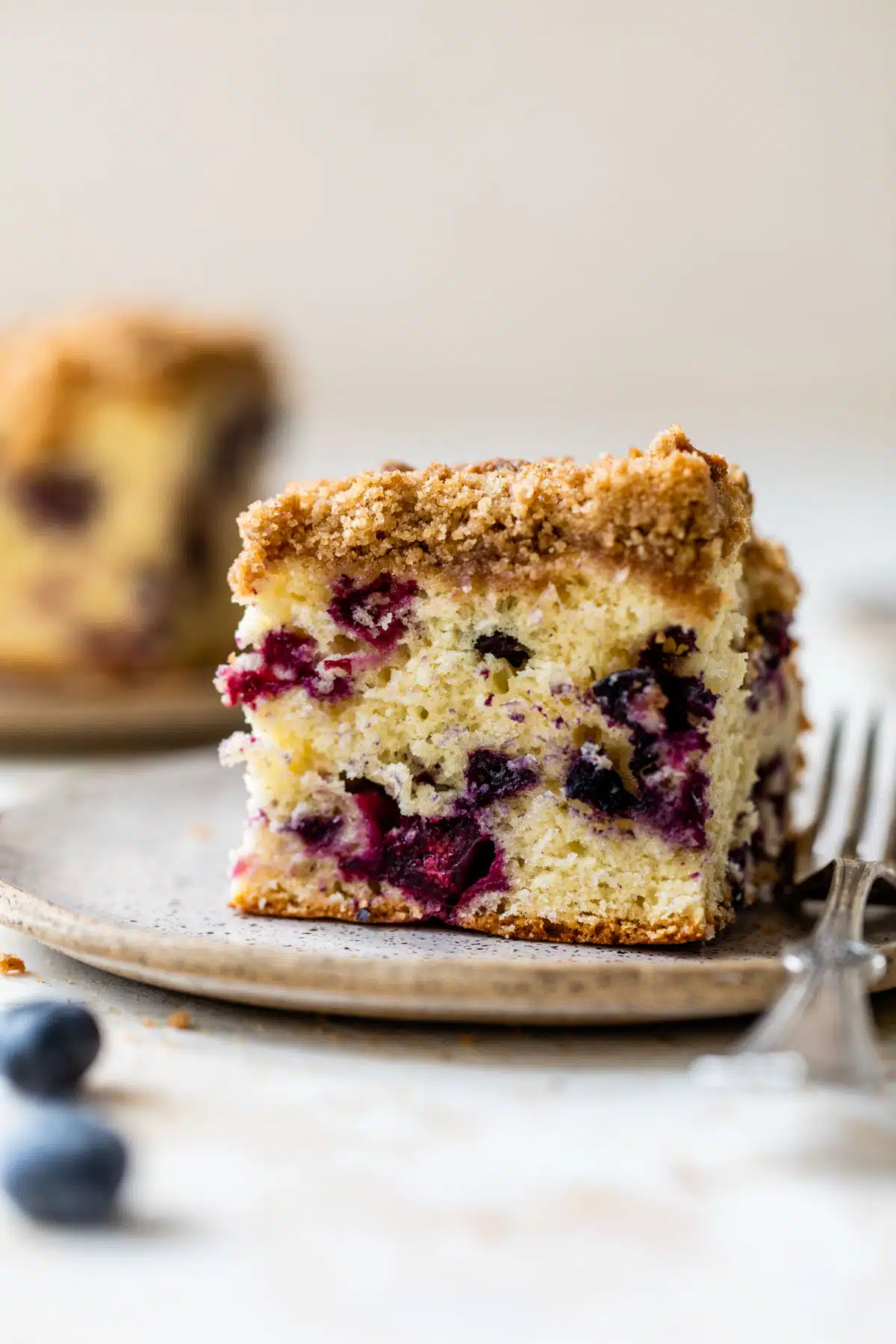 a piece of coffee cake with blueberries on a plate with a fork