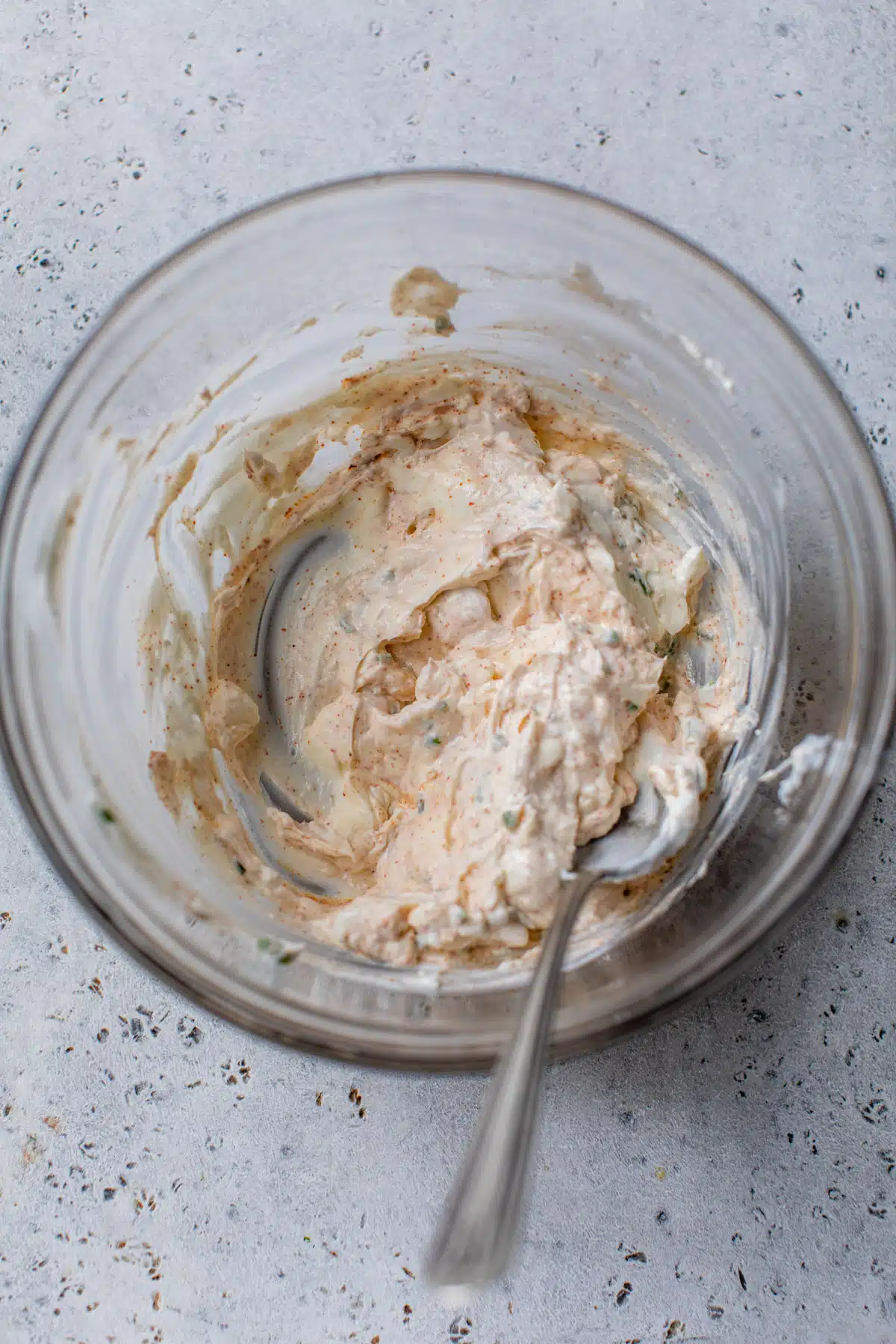 cream cheese, greek yogurt and spices mixed together in a glass bowl with a spoon