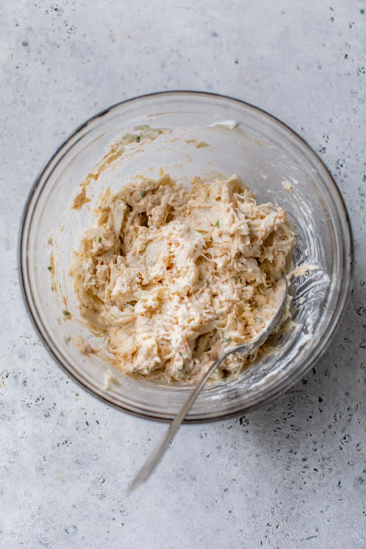 crab meat added to the greek yogurt mixture in a glass bowl with a spoon
